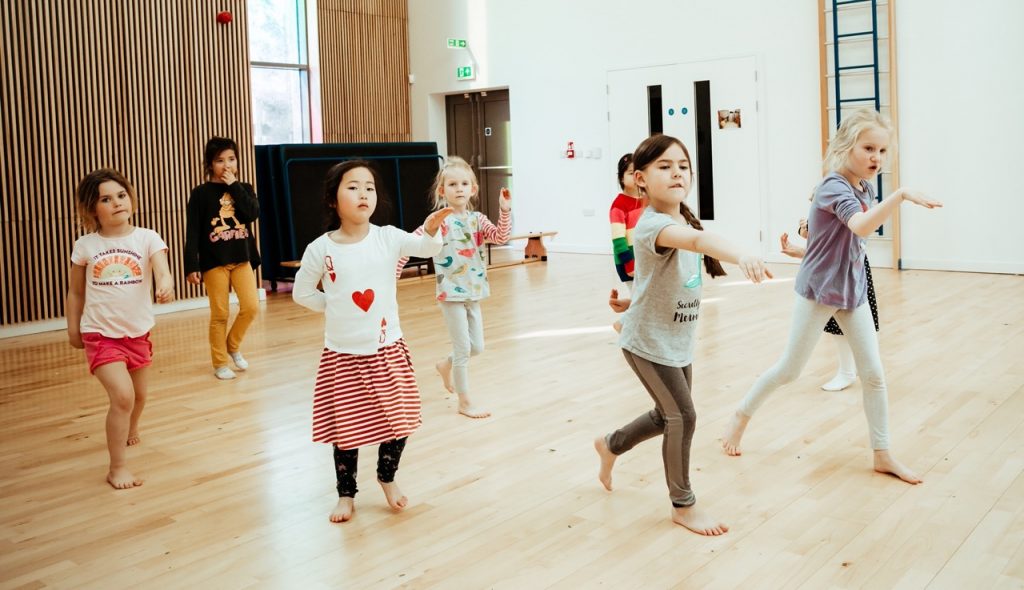 Is Dance a Sport? The Benefits for Kids 5 Pupils pointing their hands forward in the middle of a dance class
