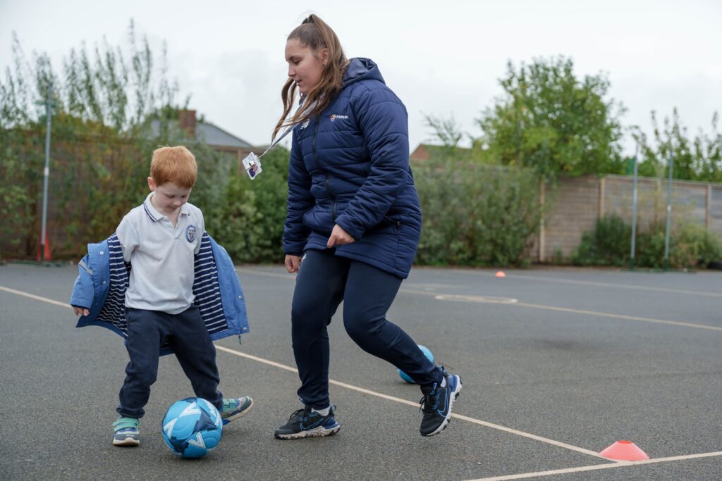 Child and sports coach playing football