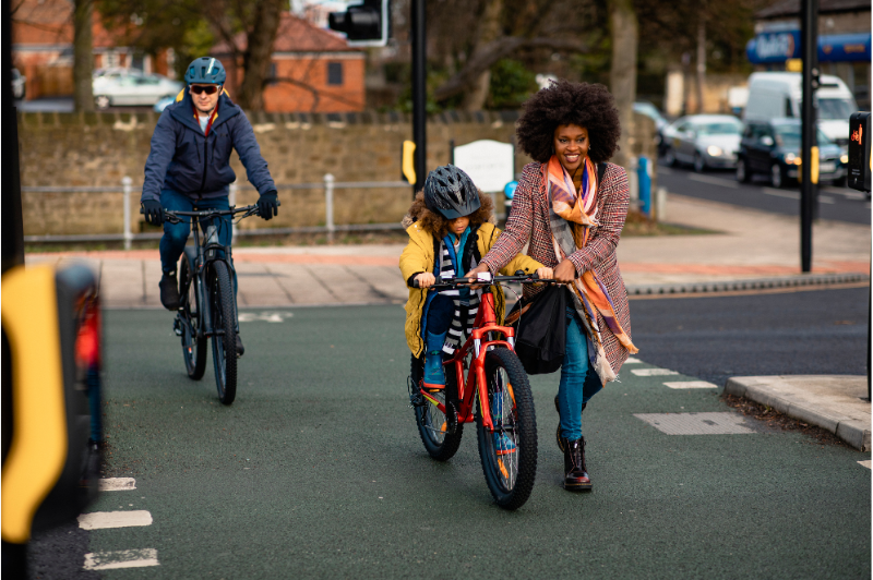 Woman helping child on bike cross the road at traffic lights