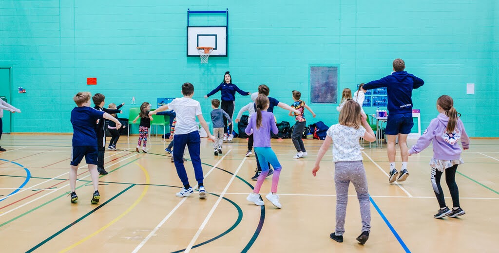 Children dancing in a sports hall with coaches